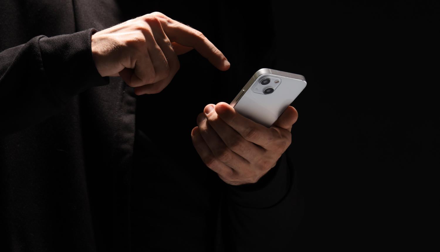 Uz melna fona redzamas personas rokas ar telefonu