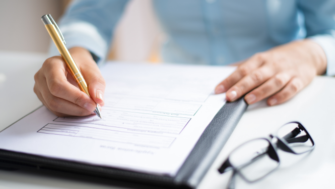 brilles, dokumentu mape un rakstoša cilvēka roka