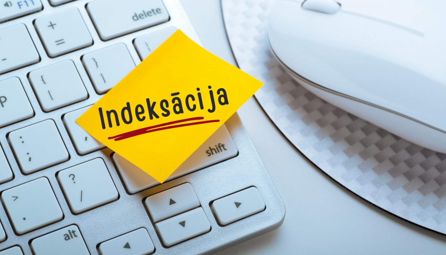Daļa no baltas klaviatūras un datorpeles. Uz klaviatūras uzlīmēta dzeltena lapa ar vārdu – Indeksācija.